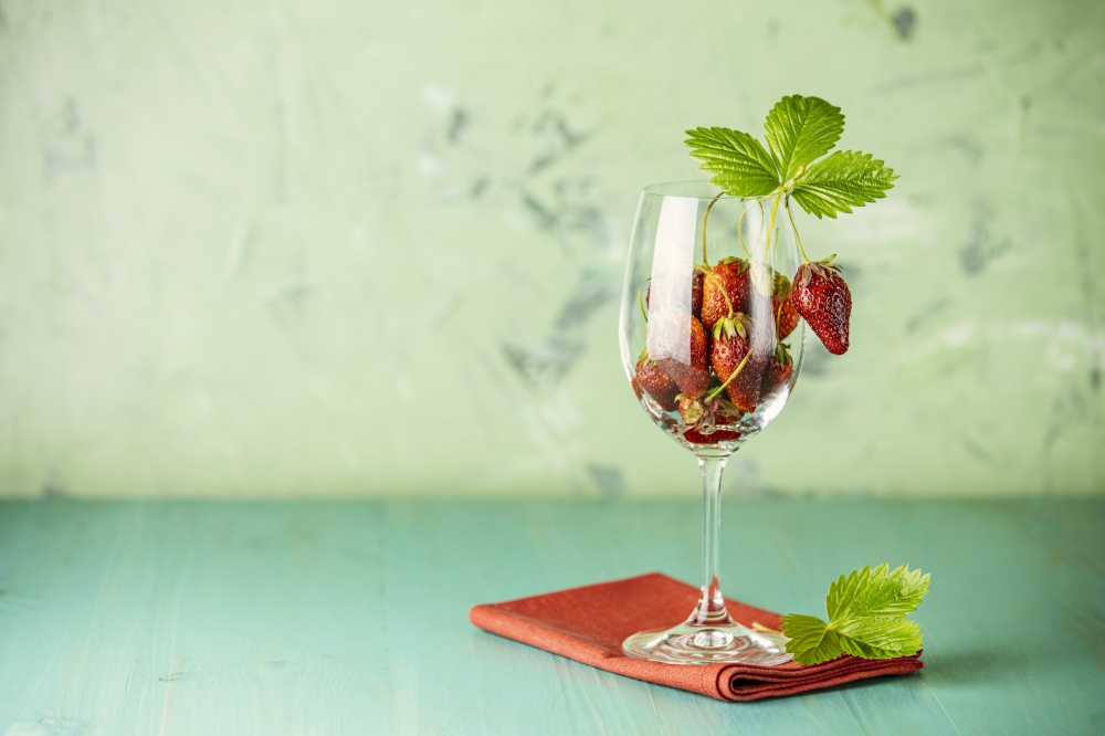 Fresh ripe raw strawberry with green leaves in the wine glass on green surface.