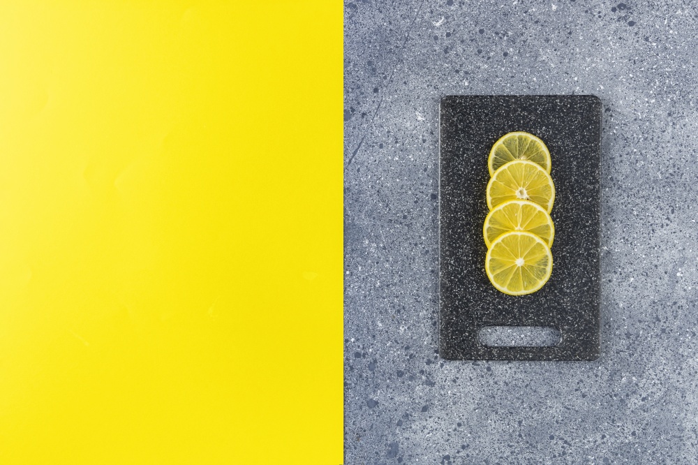 Creative food background of Ultimate Gray and Illuminating trending color. Lemon and cutting board on gray and yellow table surface