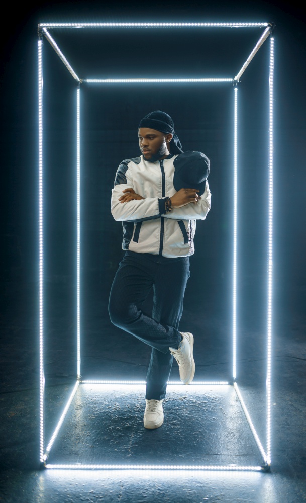 Rapper posing in illuminated cube, dark background. Hip-hop performer, rap singer, break-dance performing, entertainment lifestyle, breakdancer. Rapper posing in illuminated cube, dark background