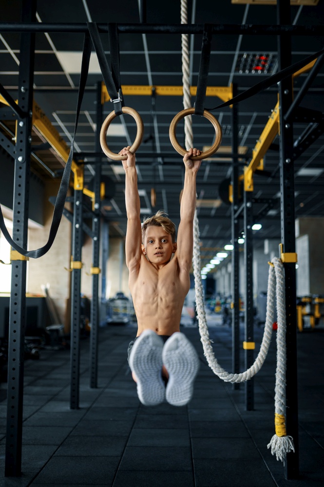 Boy doing exercise on rings in gym. Youngster on training in sport club, healthcare and healthy lifestyle, schoolboy on workout, sportive youth. Boy doing exercise on rings in gym
