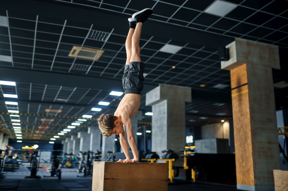 Athletic boy standing on his hands, balance exercise on pedestal in gym. Youngster on training in sport club, healthcare and healthy lifestyle, schoolboy on aerobics workout, sportive youth. Boy standing on his hands, balance exercise in gym