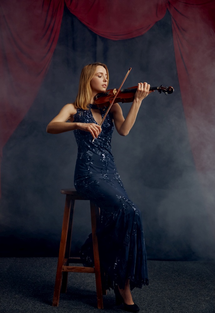 Female violonist with bow and violin, solo concert on stage. Woman with string musical instrument, musician play on viola, dark background. Female violonist with bow and violin, solo concert
