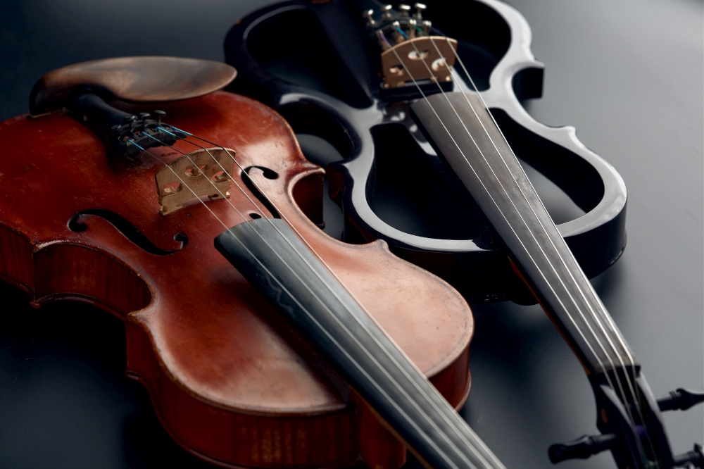 Wooden retro violin and modern electric viola, closeup view, nobody. Two classical string musical instruments, black background. Wooden retro violin and modern electric viola
