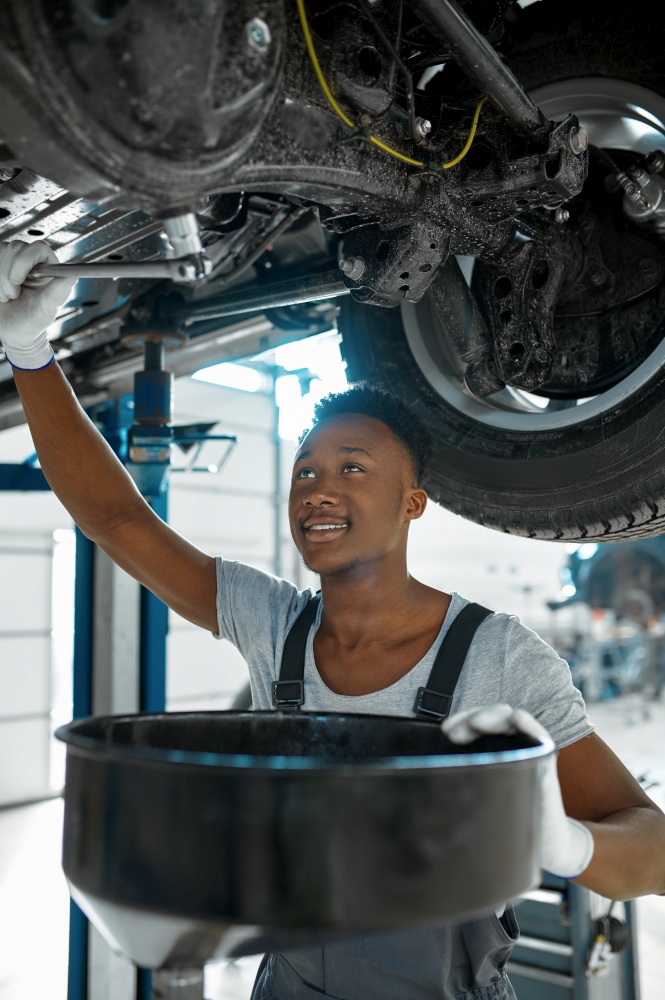 Male mechanic drains the oil, car service. Vehicle repairing garage, man in uniform, automobile station interior on background. Male mechanic drains the oil, car service