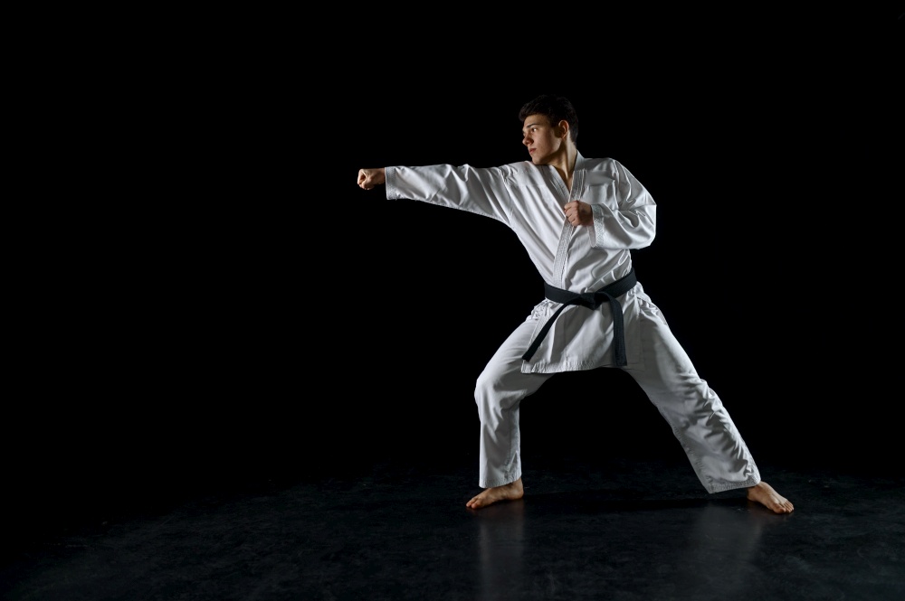 Male karate fighter in white kimono, combat stance, dark background. Man on karate workout, martial arts, fighting competition. Male karate fighter in white kimono, combat stance