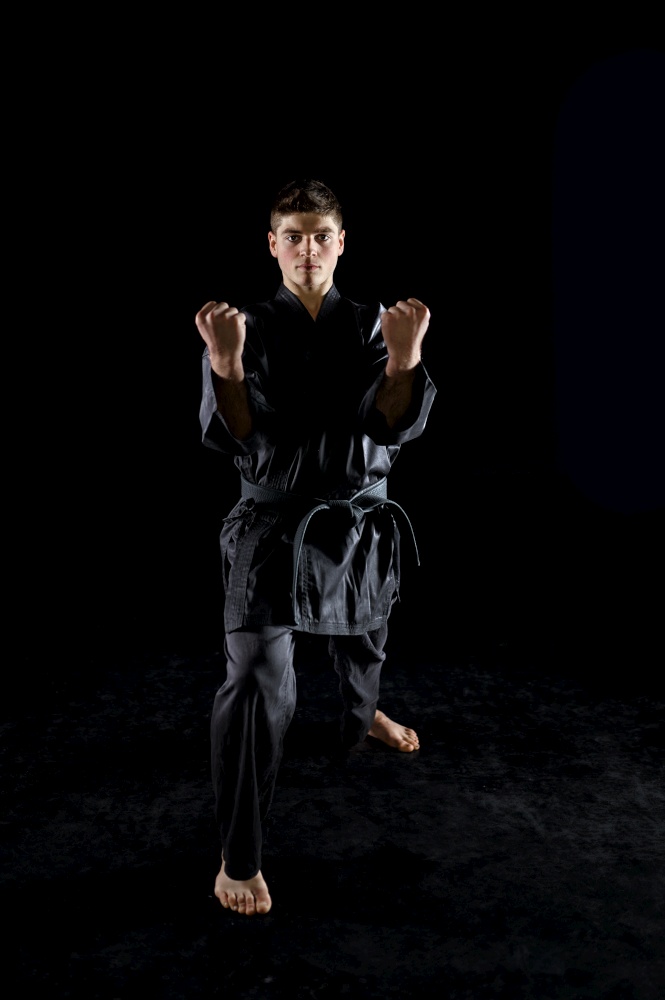 Male karate fighter in black kimono, combat stance, front view, dark background. Man on workout, martial arts, fighting competition. Male karate fighter in black kimono, front view