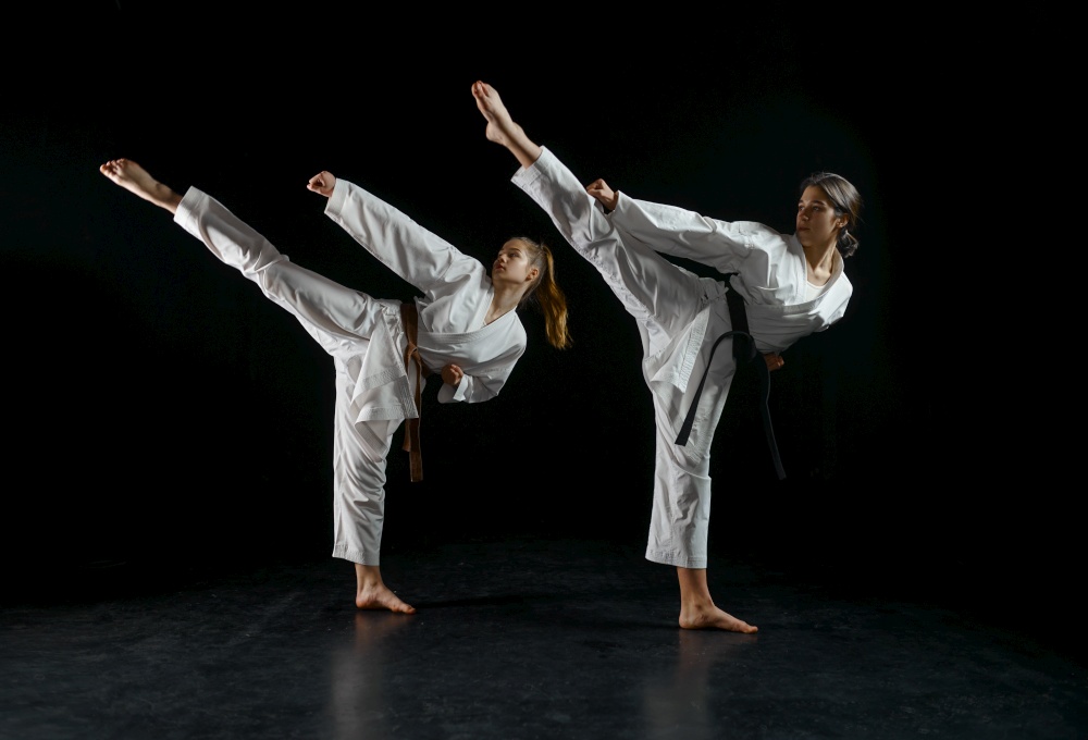 Female karatekas in white kimono, combat stance in action, dark background. Karate fighters on workout, martial arts, women fighting competition. Female karatekas in kimono, combat stance