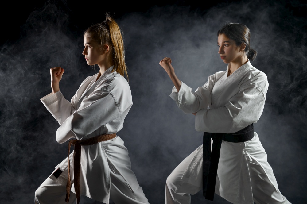 Female karatekas, training in white kimono, combat stance in action, dark background. Karate fighters on workout, martial arts, women fighting competition. Female karatekas, training in white kimono