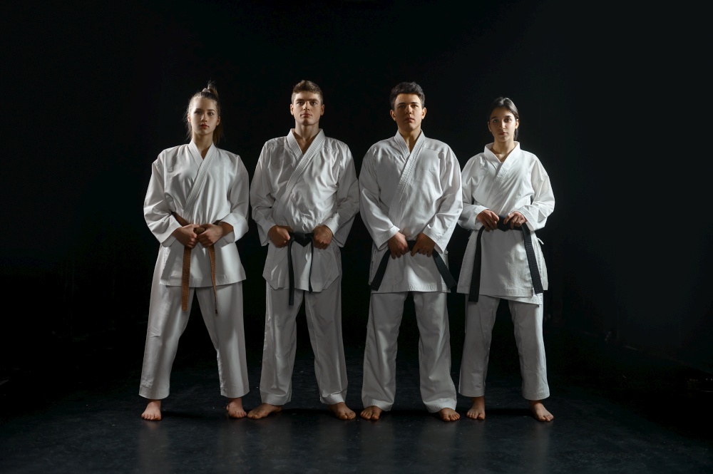 Four karatekas in white kimono, group training, dark background. Karate fighters on workout, martial arts, fighting competition. Four karatekas in white kimono, group training