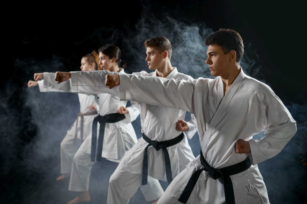 Four karate fighters poses in white kimono, group training, dark smoky background. Karatekas on workout, martial arts. Four karate fighters poses in white kimono