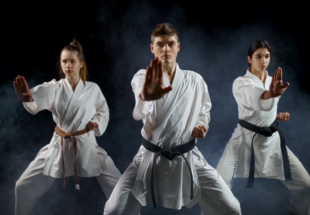 Female karate fighters, training with master in white kimono, dark smoky background. Karatekas on workout, martial arts, fighting competition. Female karate fighters, training with master