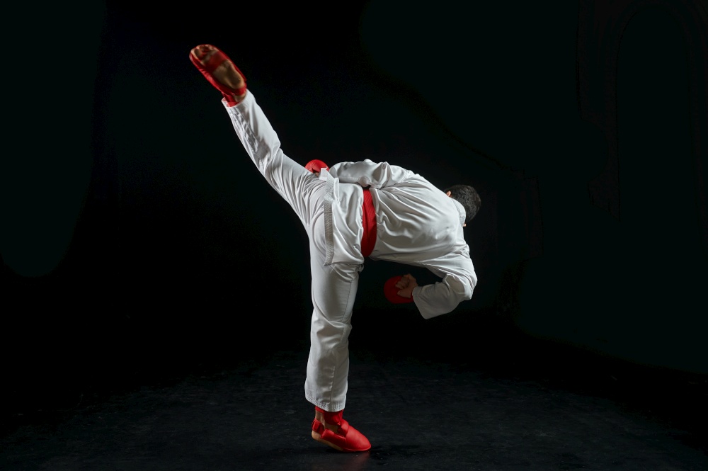 Male karateka, fighter practice in white kimono and red gloves, combat stance, dark background. Man on karate workout, martial arts, training before fighting competition. Karateka, fighter in white kimono and red gloves