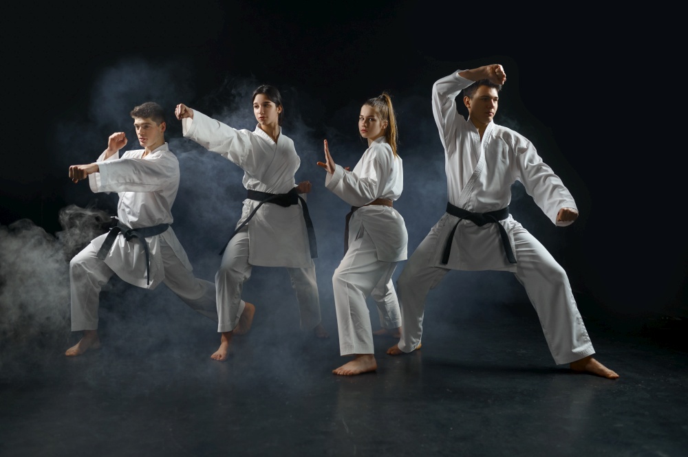 Four karate fighters in white kimono poses in combat stances, group training, dark smoky background. Karatekas on workout, martial arts, fighting competition. Karate fighters in kimono poses in combat stances