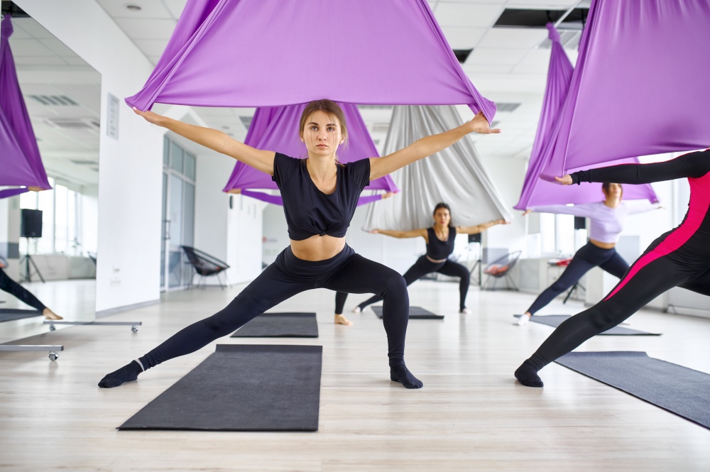 Fly yoga, female group training with hammocks. Fitness, pilates and dance exercises mix. Women on yogi workout in sports studio. Fly yoga, female group training with hammocks