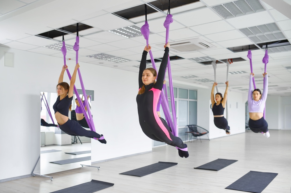 Fly anti-gravity yoga, female group training with hammocks. Fitness, pilates and dance exercises mix. Women on yoga workout. Anti-gravity yoga, group training with hammocks