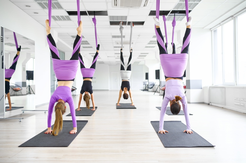 Aerial yoga class, female group training, hanging on hammocks. Fitness, pilates and dance exercises mix. Women on yogi workout in sports studio. Aerial yoga class, hanging on hammocks
