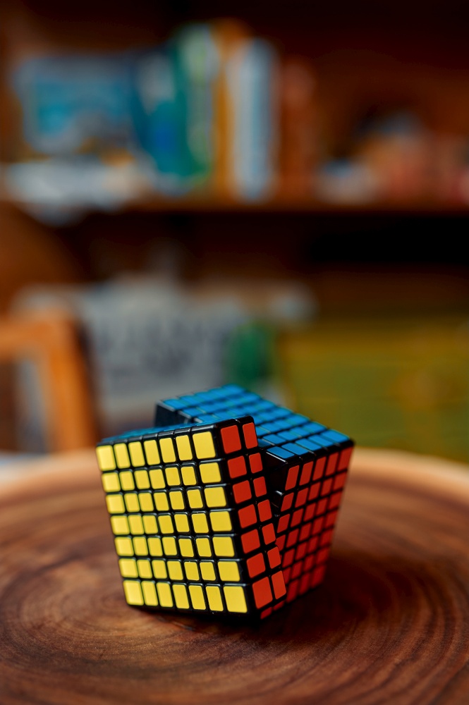 Colorful puzzle cube 7x7 on wooden stump, closeup view, nobody. Toy for brain and logical mind training, creative game, solving of complex problems. Puzzle cube 7x7 on wooden stump, closeup view