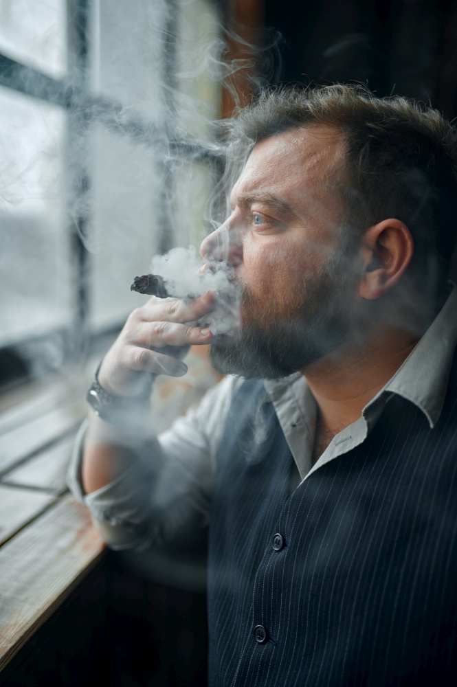Man at the windowsill and smokes a cigar, vintage office interior on background. Tobacco smoking culture, specific flavor. Male smoker looks at the window. Man at the windowsill and smokes a cigar