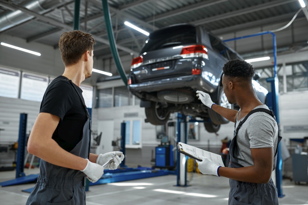 Two male mechanics talking in car service. Vehicle repairing garage, men in uniform, automobile station interior on background. Professional auto diagnostic. Two male mechanics talking in car service