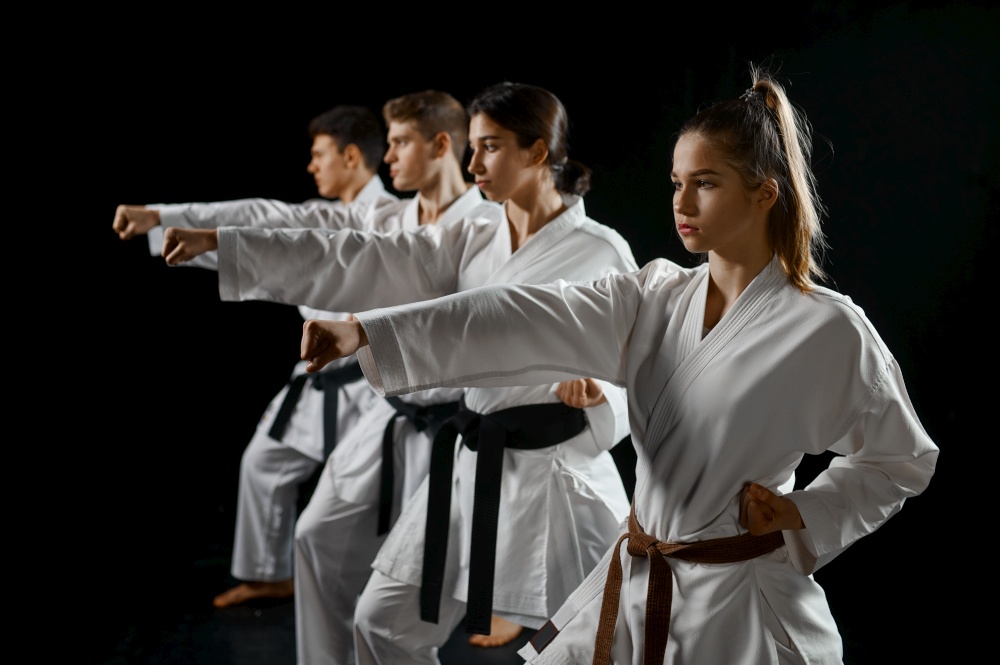 Four karate fighters poses in white kimono, group training, dark smoky background. Karatekas on workout, martial arts, fighting competition. Four karate fighters poses in white kimono