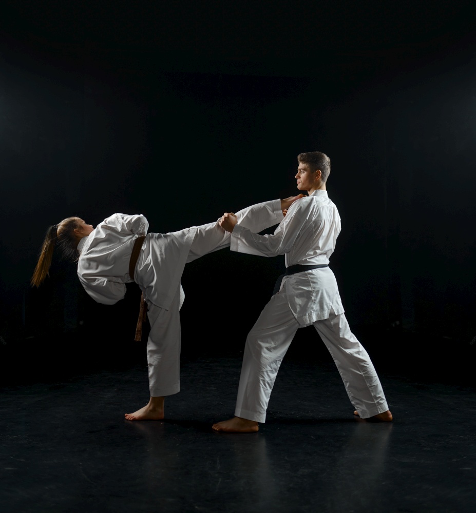 Female karate fighter on training with male master, white kimono, dark smoky background. Karateka on workout, martial arts, fighting competition. Female karate fighter on training with male master