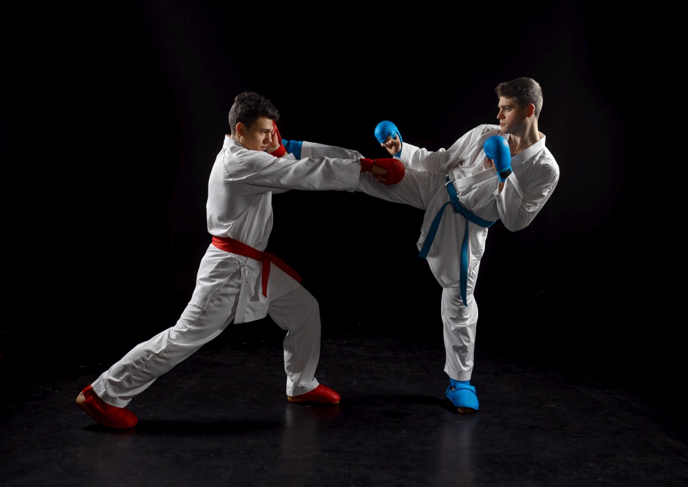 Two male karatekas in white kimono and gloves, strike in action, dark background. Fighters on workout, martial arts, fighting competition. Two karatekas in white kimono and gloves, strike