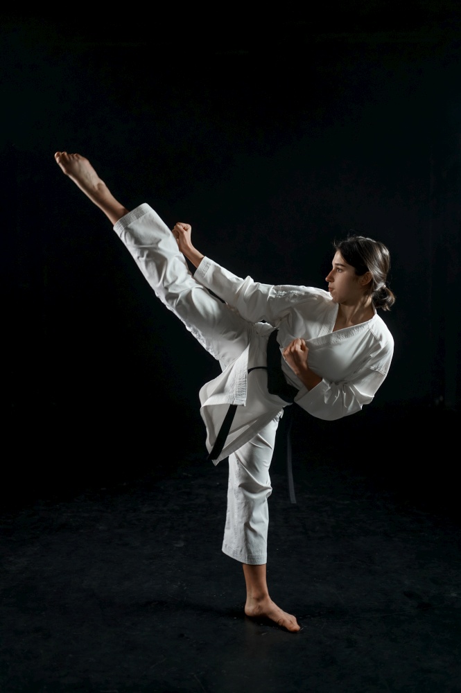 Male karate fighter in white kimono, combat stance in action, dark background. Karateka on workout, martial arts, training before fighting competition. Male karate fighter, combat stance in action