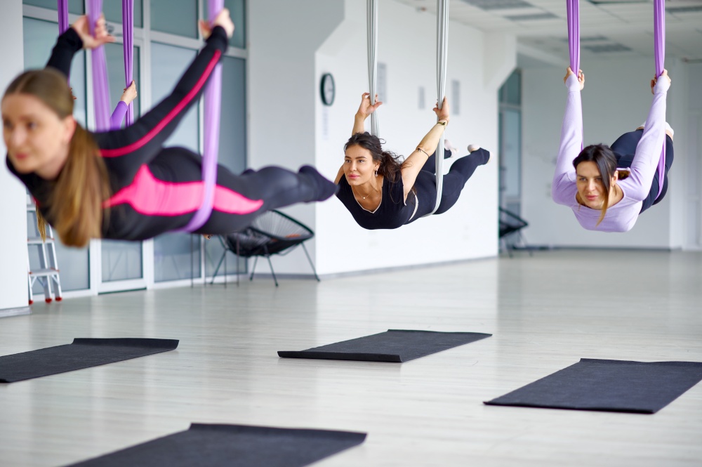Fly anti-gravity yoga, female group training with hammocks. Fitness, pilates and dance exercises mix. Women on yoga workout in sports studio. Anti-gravity yoga, group training with hammocks