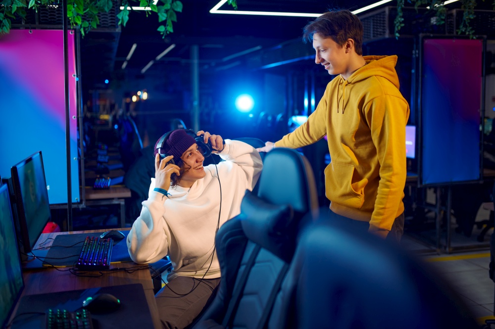 Two young gamers talking at the monitor in gaming club. Virtual entertainment, e-sport tournament, cybersport lifestyle. Male people leisures in internet cafe. Two gamers talking at the monitor in gaming club