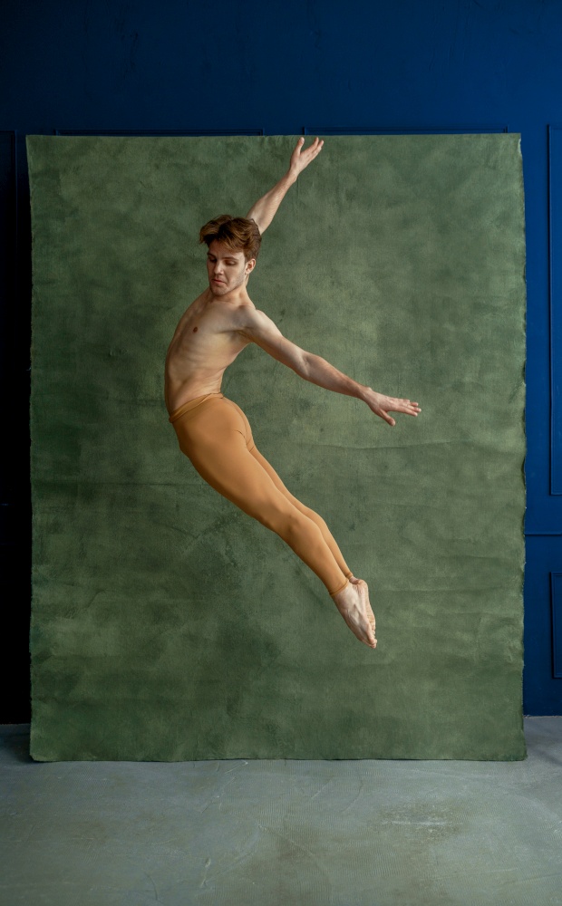 Male ballet dancer jumps in dancing studio, grunge wall on background. Performer with muscular body, grace and elegance of movements. Male ballet dancer jumps in dancing studio