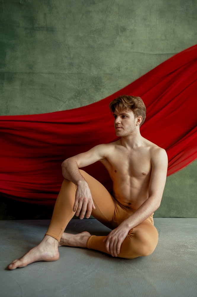 Male ballet dancer, dancing studio, grunge wall and red cloth on background. Performer with muscular body, grace and elegance of movements. Male ballet dancer, dancing studio, grunge wall