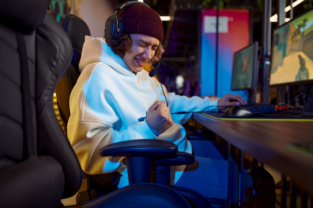 Young gamer in headphones play in game club. Virtual entertainment, e-sport tournament, cybersport lifestyle. Male person leisures in internet cafe. Young gamer in headphones play in game club