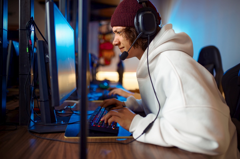 Young gamer in headset play shooter in game club. Virtual entertainment, e-sport tournament, cybersport lifestyle. Male person leisures in internet cafe. Young gamer in headset play shooter in game club