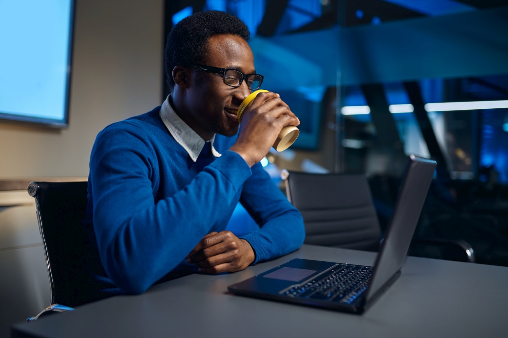 One manager in glasses works on laptop in night office. Male worker, dark business center interior on background, modern workplace. Manager in glasses works on laptop in night offic