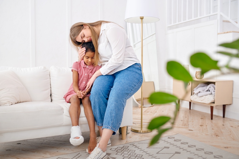 Mother feels sorry for her little daughter on sofa in living room.Mom and female child leisures in their house together, good relationship, parental care and love. Mother feels sorry for her little daughter