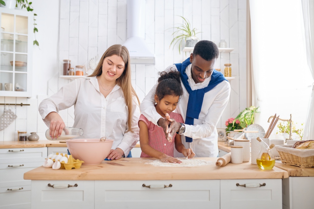 Happy family cooking cakes on breakfast in the kitchen. Mother, father and their daughter prepares the dough in the morning, good relationship. Happy family cooking cakes on breakfast in kitchen