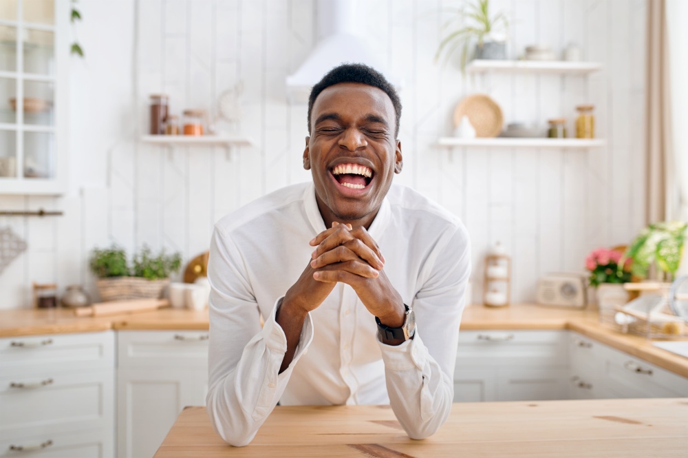 Laughing man sitting at the counter on the kitchen. Cheerful male person poses at the table at home in the morning, happy lifestyle. Laughing man sitting at the counter on kitchen