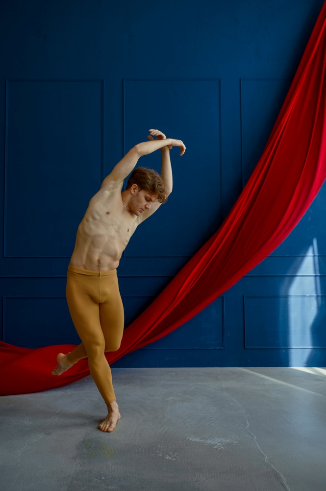 Male ballet dancer, training in dancing class, blue walls and red cloth on background. Performer with muscular body, grace and elegance of movements. Male ballet dancer, training in dancing class