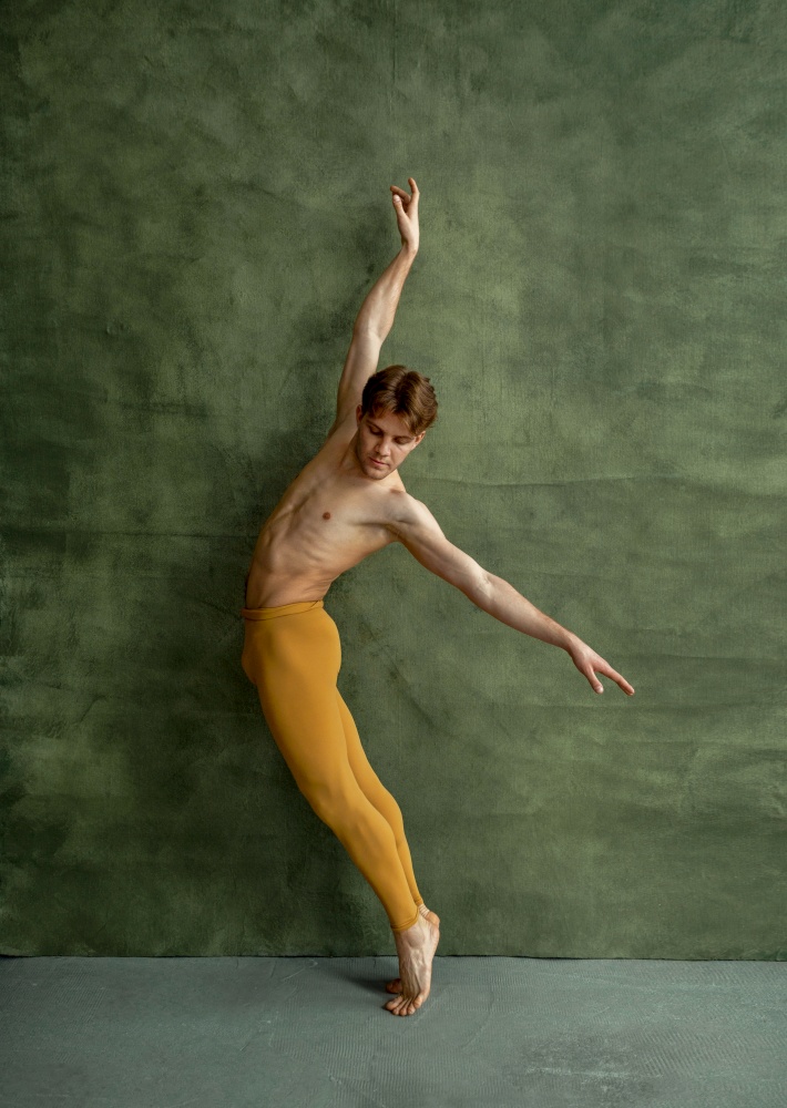 Male ballet dancer, training in dancing class, grunge wall on background. Performer with muscular body, grace and elegance of movements. Male ballet dancer, training in dancing class