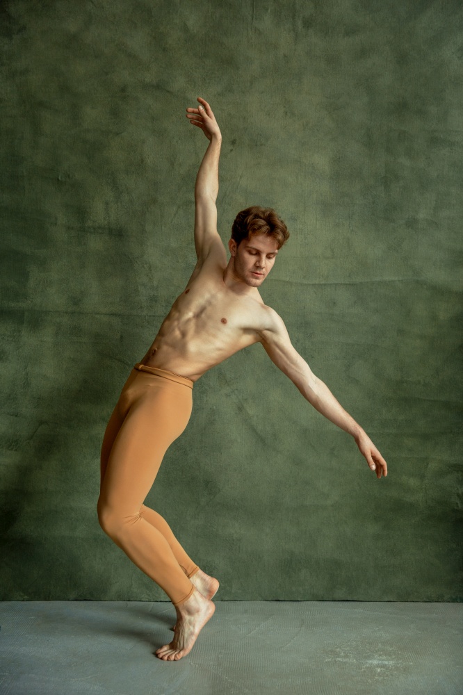 Male ballet dancer poses at grunge wall in dancing studio. Performer with muscular body, grace and elegance of dance. Ballet dancer poses at grunge wall, dancing studio