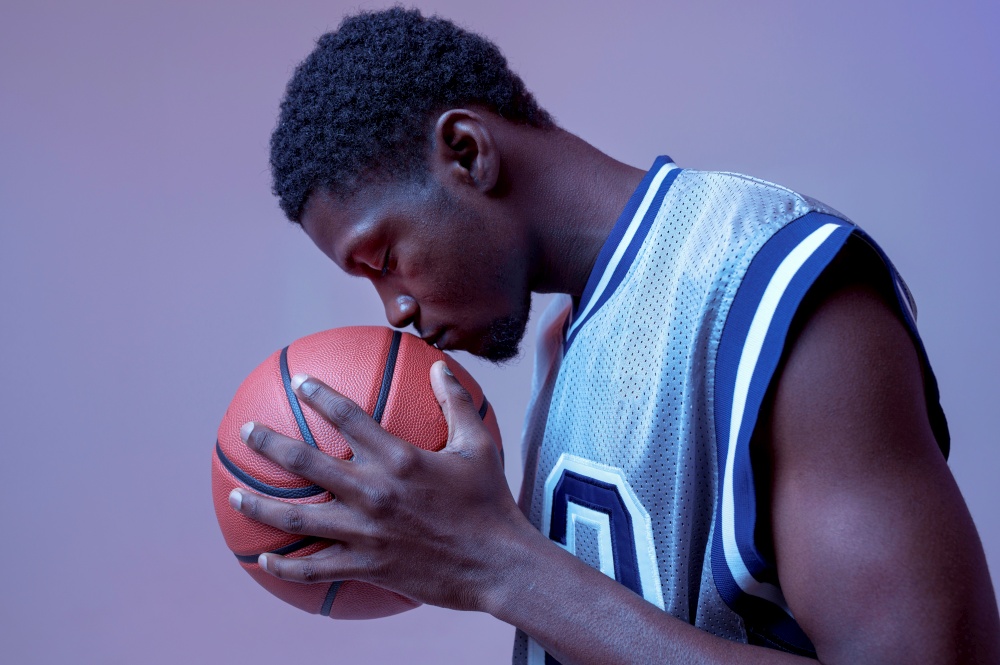 Serious basketball player poses with ball in studio, neon background. Professional male baller in sportswear playing sport game, tall sportsman. Serious basketball player with ball in studio