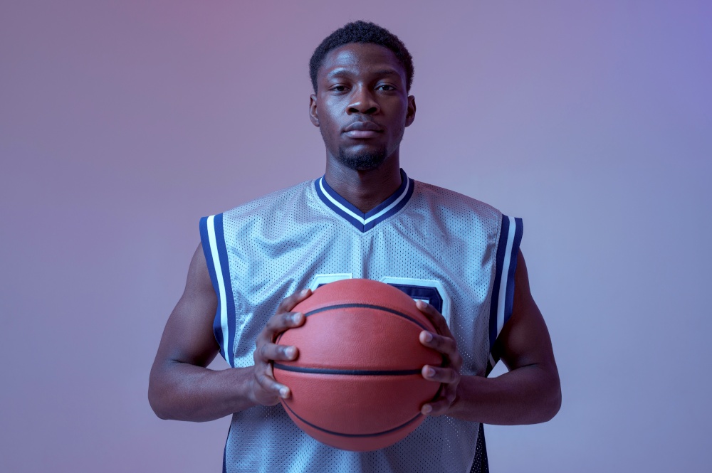 Confident basketball player poses with ball in studio, neon background. Professional male baller in sportswear playing sport game, tall sportsman. Confident basketball player poses with ball