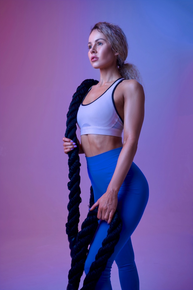 Young sportswoman with ropes poses in studio. Fitness woman at the photo shoot, sport concept, active lifestyle. Young sportswoman with ropes poses in studio
