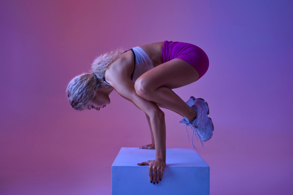 Sportswoman doing balance exercise in studio, neon background. Fitness woman at the photo shoot, sport concept, active lifestyle motivation. Sportswoman doing balance exercise in studio