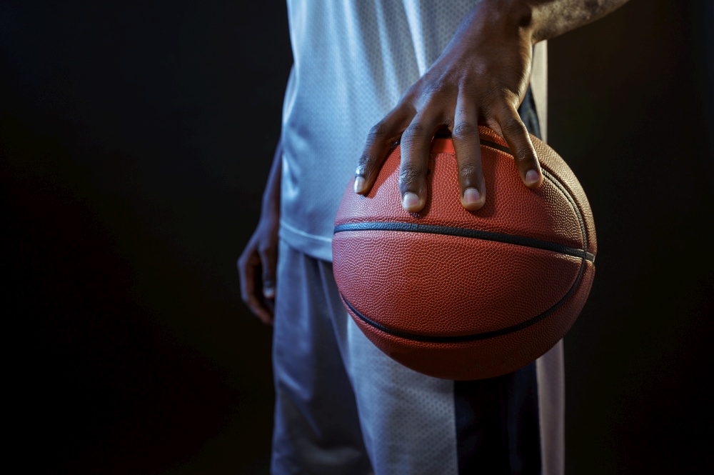 Strong basketball player hand holds ball in studio, black background. Professional male baller in sportswear playing sport game, tall sportsman. Basketball player holds ball, black background