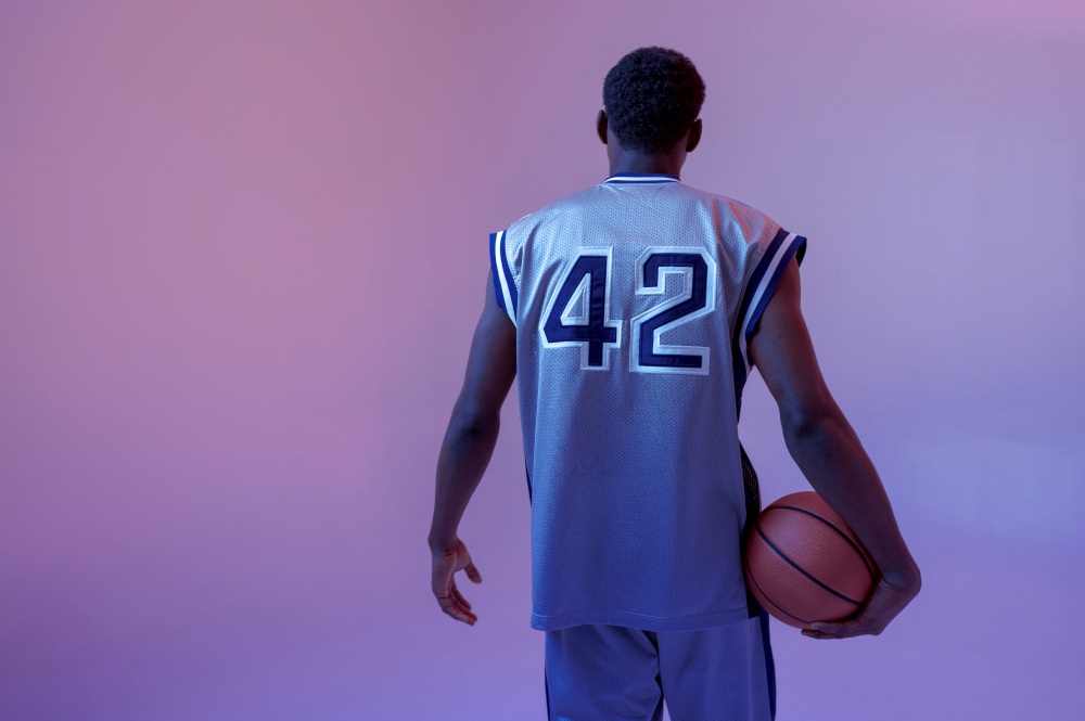 Basketball player poses with ball in studio, back view. Professional male baller in sportswear playing sport game, tall sportsman. Basketball player with ball, black background