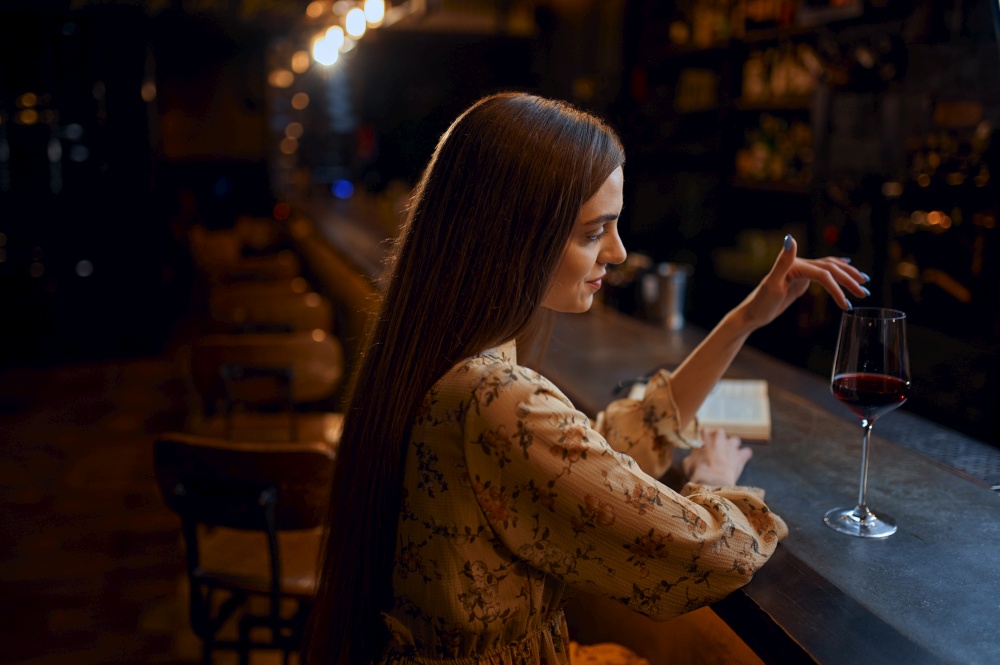 Alone young woman with glass of red wine sitting at the counter in bar. One female person in pub, human emotions, leisure activities, nightlife. Alone woman with glass of wine sitting in bar