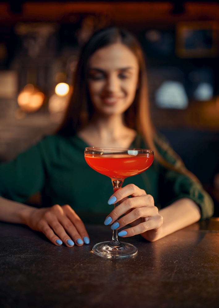 Smiling woman drinks coctail at the counter in bar. One female person in pub, human emotions, leisure activities, nightlife. Smiling woman drinks coctail at the counter in bar