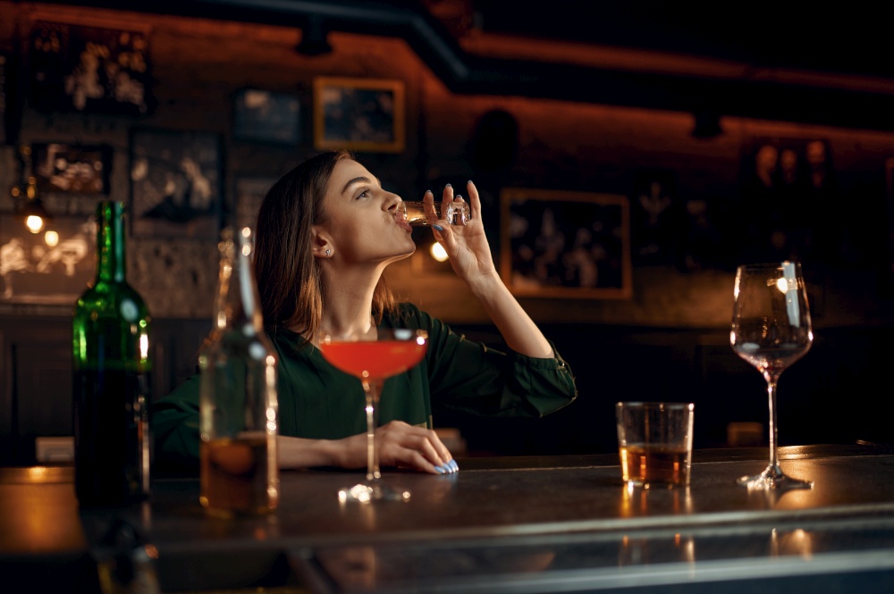 Stressed woman drinks different alcohol at the counter in bar. One female person in pub, human emotions, leisure activities, nightlife. Stressed woman drinks alcohol at counter in bar