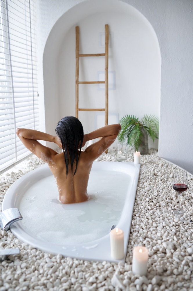 Attractive young woman relax in a bubble bath, back view. Female person in bathtub, beauty and health care in spa, wellness treathment in bathroom. Attractive woman relax in a bubble bath, back view